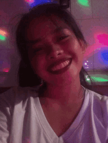 a girl in a white shirt is smiling in front of a wall of lights