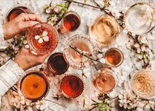 a person is holding a glass of wine on a table surrounded by glasses of wine and flowers .