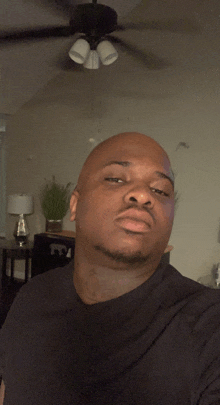 a man in a black shirt is taking a selfie in front of a ceiling fan