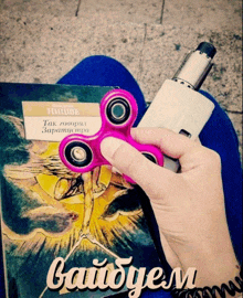 a person holding a pink fidget spinner on top of a book titled " byobem "