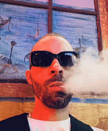 a man with a beard wearing sunglasses is blowing smoke from his mouth