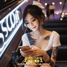 a woman wearing glasses is looking at her phone in front of a sign for museum bola