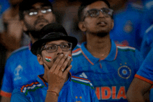 a man covering his mouth with his hand while wearing a blue india shirt