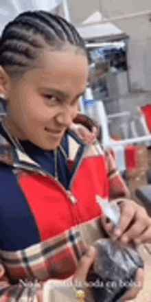 a young boy with braids is sitting at a table holding a bottle .