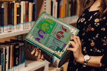 a woman is holding a book with a green cover and a gold frame