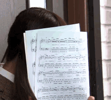 a woman holds a sheet of music in front of her face with the letters a and d on it