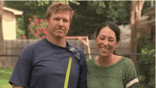 a man and a woman are standing next to each other in a backyard and smiling for the camera .