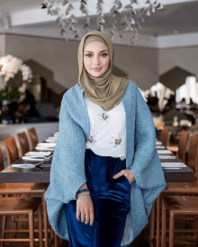 a woman wearing a hijab stands in front of a long table