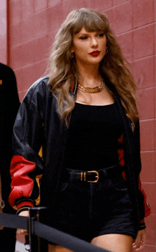 a woman wearing a black jacket and shorts is standing in front of a brick wall