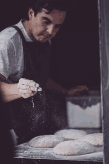 a man in an apron is sprinkling flour on a tray of dough