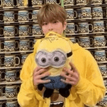 a man is holding a stuffed minion in front of a wall of mugs .