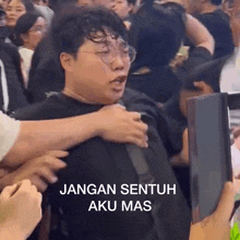 a man with glasses is being held by someone in a crowd with the caption jangan sentuh aku mas .