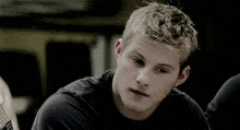 a young man in a black shirt is sitting in a dark room and looking at the camera .