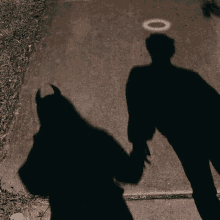 shadows of a devil and an angel holding hands on a sidewalk