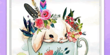 a rabbit is laying in a teacup with flowers and feathers on its head .