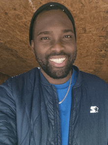 a man wearing a blue shirt and a blue starter jacket smiles