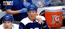 a hockey player wearing a blue helmet is sitting in the stands with a gatorade cooler in front of him .