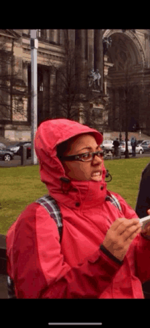 a woman wearing a pink jacket and glasses holds a cell phone