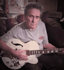 a man sitting on a couch holding a guitar with a chevrolet logo on his shirt