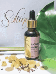 a bottle of liquid gold beauty oil next to a green leaf