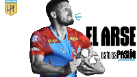 a man in a red and blue jersey holds a soccer ball in front of a sign that says el arse