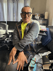 a man wearing glasses sits on a couch next to a bible and a box of kleenex