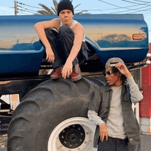 a man is sitting on top of a tractor tire next to another man .