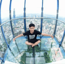 a young man is sitting on a glass floor in a ferris wheel overlooking a city .