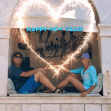 a man and a woman are sitting on a window sill with sparklers in the shape of a heart and the words happy new year