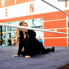 a woman is laying on the floor in a wrestling ring with the letters e and n visible in the background