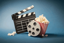 a clapper board a film reel and a striped bucket of popcorn on a blue background