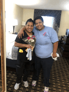 two women are posing for a picture in a hotel room and one of them is wearing a shirt that says breast cancer awareness month