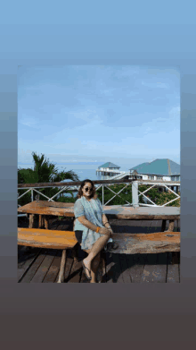 a woman is sitting on a wooden bench with a view of the ocean