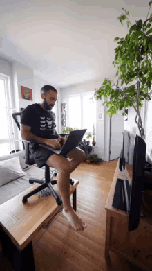 a man is sitting on a chair using a laptop and wearing a shirt that says ' skeleton ' on it