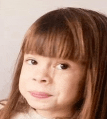 a little girl with long hair and bangs is making a face .