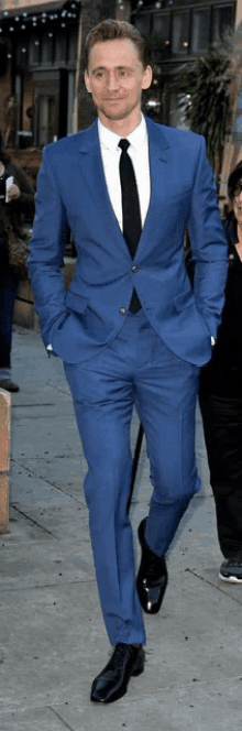 a man in a blue suit and black tie walks down a sidewalk