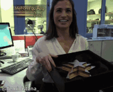 a woman holding a box with a star on it in front of a sign that says " melhores do ano "