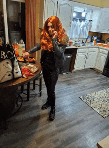 a woman in a wig stands in a kitchen next to a bag that says boo