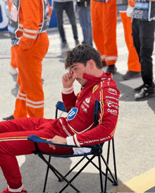 a man in a red racing suit sits in a chair