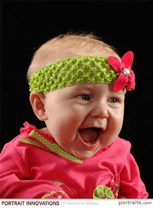 a baby wearing a green headband with a red flower on it is smiling