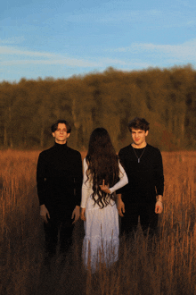 a woman in a white dress stands between two men in black shirts in a field