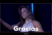 a woman is smiling in front of a sign that says gracias camara 1 on it