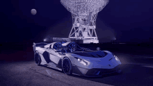 a white sports car is parked in front of a large antenna at night