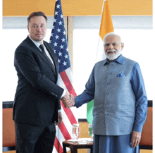 a man in a suit and tie shakes hands with another man in front of an american flag