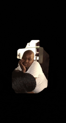 a man in a white shirt is sitting in a dark room with his hand on his face