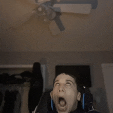 a man with his mouth open is looking up at a ceiling fan