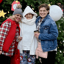 three women posing in front of a christmas tree