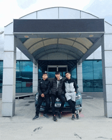 three young men are posing in front of a volkswagen with license plate number 44aa