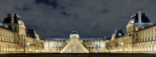 a large building at night with a pyramid in front of it