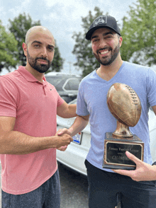 two men shaking hands while one holds a trophy that says fantasy football league